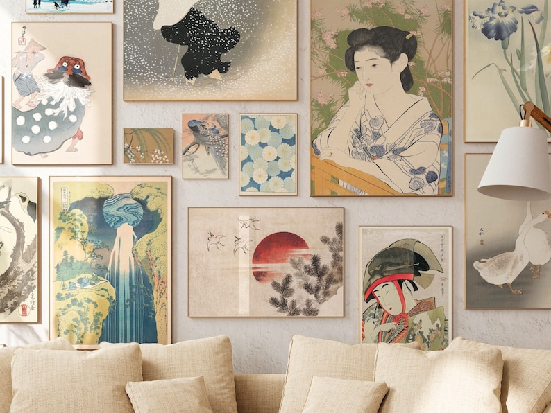 May include: A gallery wall featuring a collection of Japanese-inspired art prints. The prints depict various scenes, including a woman in traditional clothing, a waterfall, a red sun, and a bird. The prints are framed in simple wooden frames and are arranged in a symmetrical pattern on a white wall.