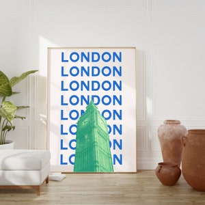 May include: A framed print with a white background and blue text that reads "LONDON" repeated multiple times. The text is stacked vertically. A green image of Big Ben is centered in the print.