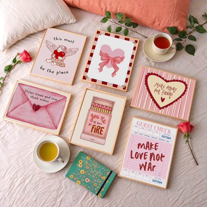 May include: A collection of framed art prints with romantic themes, including a heart with a bow, an envelope, and a matchbox with the text "you're my kind of fire." The prints are in shades of pink and red.