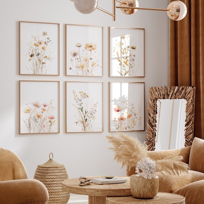 May include: Six framed watercolor prints of delicate wildflowers in shades of pink, yellow, and white, arranged in a grid on a white wall. The prints are set against a backdrop of a living room with a wicker basket, a fluffy pampas grass, and a brown couch.
