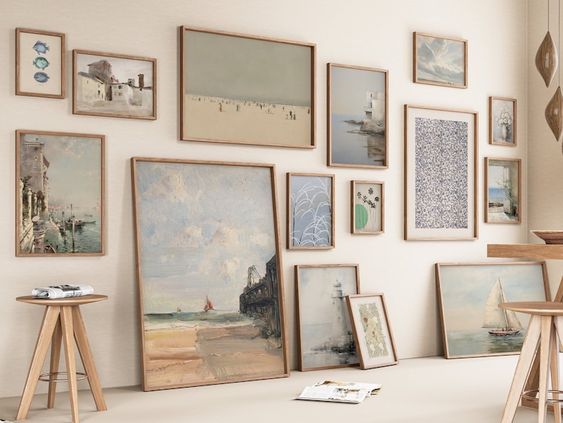 Puede incluir: Una pared de galer&iacute;a con una variedad de obras de arte enmarcadas, incluyendo paisajes, marinas y dise&ntilde;os abstractos. La pared est&aacute; pintada de un color beige claro y los marcos son todos de madera.