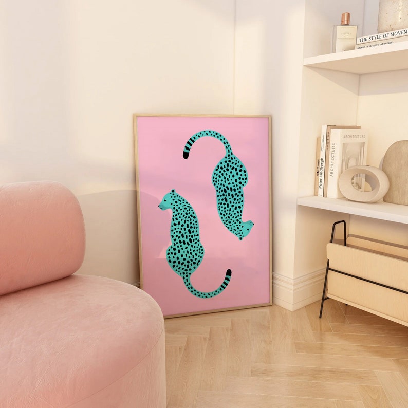 May include: A framed print with a pink background featuring two turquoise cheetahs with black spots. The cheetahs are facing opposite directions and are in a curved shape.