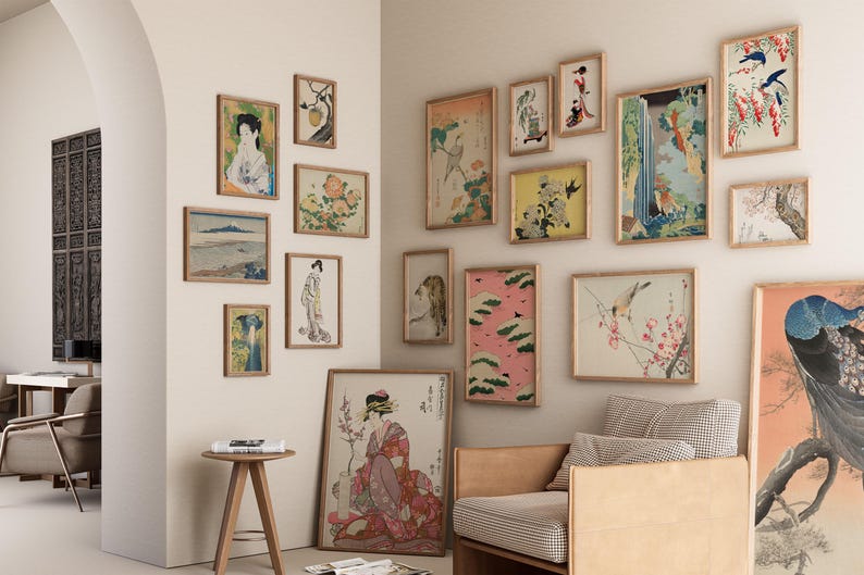 May include: A white wall with a collection of framed artwork featuring Japanese-inspired prints and paintings. The artwork includes images of birds, flowers, landscapes, and people. The frames are all made of wood and have a natural finish.