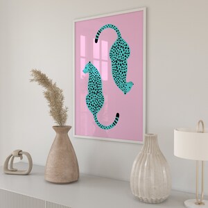 May include: A framed print with a pink background featuring two turquoise cheetahs with black spots. The cheetahs are facing opposite directions and are in a curled position.