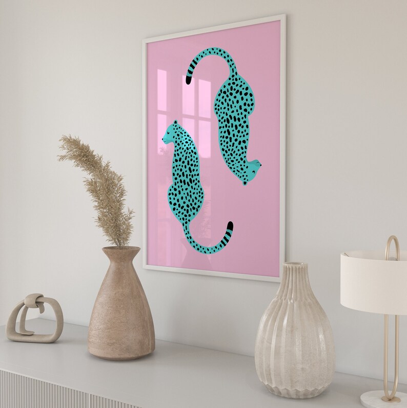 May include: A framed print with a pink background featuring two turquoise cheetahs with black spots. The cheetahs are facing opposite directions and are in a curled position.
