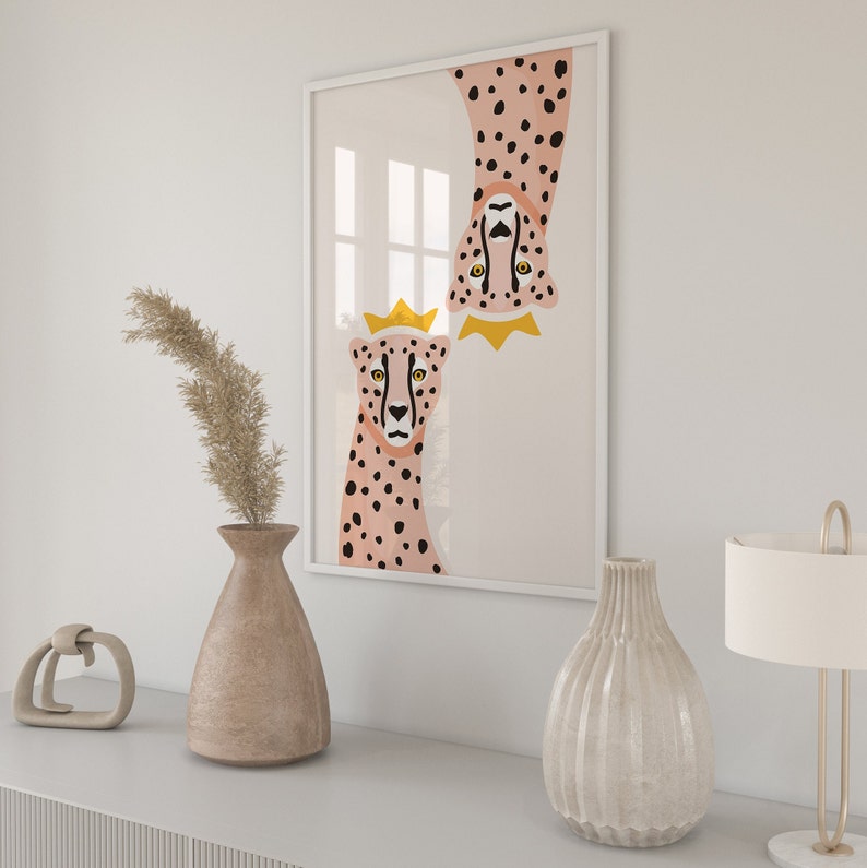 May include: A framed print featuring two pink and black cheetahs with gold crowns. The cheetahs are facing the viewer, with one upside down. The print is on a white background.