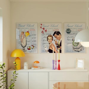 May include: Three vintage guest check style prints with illustrations of cocktails and people. The prints are framed and hung on a white wall above a white shelf with a yellow lamp, a stack of books, and a candle holder with three candles.