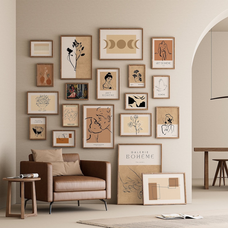 May include: A gallery wall with a variety of framed prints in black and white and brown tones. The prints feature abstract designs, line art, and minimalist illustrations. The prints are arranged in a grid pattern on a light beige wall.