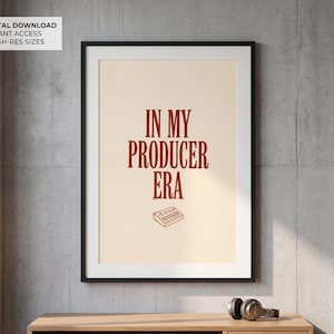 May include: A framed wall art print featuring a cream-colored background with the dark red text IN MY PRODUCER ERA centered in a bold serif font. Below the text is a simple line drawing of a music production synthesizer or drum machine.