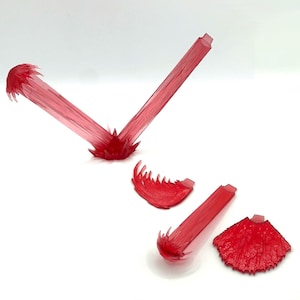 May include: A set of translucent red plastic action figure effect pieces. The collection includes two long beam-like structures, one curved jagged piece, and one fan-shaped textured piece, all designed to simulate energy blasts or explosive impacts.