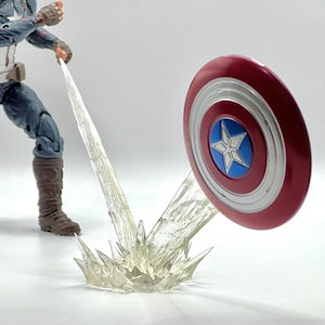 Puede incluir: Figura de acción del Capitán América con un escudo rojo, blanco y azul. El escudo está en movimiento, con un efecto de energía de plástico transparente que emana de él. La figura está en una pose dinámica, sugiriendo acción.