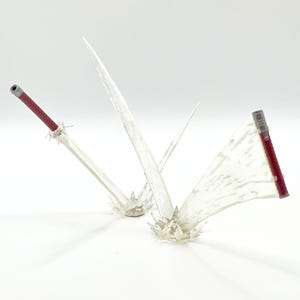 May include: Clear plastic sword props with red handles and textured grips. The swords are mounted on clear, spiky bases. The image is set against a white background.
