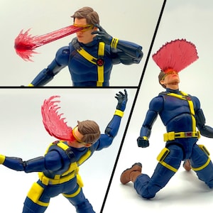 May include: A posable action figure of a character wearing a dark blue tactical suit with yellow straps, a yellow belt, and a red X-logo. The figure features a yellow visor and a translucent red plastic piece simulating an energy beam blast.