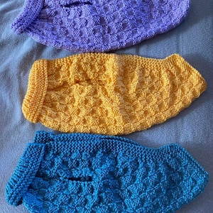 May include: Three knitted dog sweaters in different colours: purple, yellow and blue. Each sweater has a textured pattern.