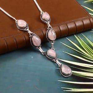 Puede incluir: Un collar de plata con cinco piedras de color rosa en forma de lágrima. Las piedras están engastadas en plata y tienen un aspecto delicado y femenino.