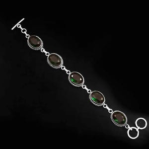 May include: A silver bracelet with five oval-shaped green gemstones. The bracelet has a T-bar clasp and a toggle clasp.