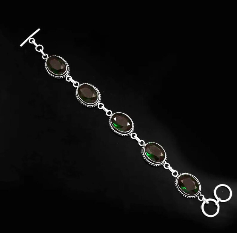 May include: A silver bracelet with five oval-shaped green gemstones. The bracelet has a T-bar clasp and a toggle clasp.