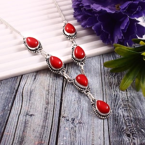 Puede incluir: Un collar de plata con gotas de piedras preciosas rojas. El collar tiene una cadena delicada y presenta cinco piedras en forma de gota.