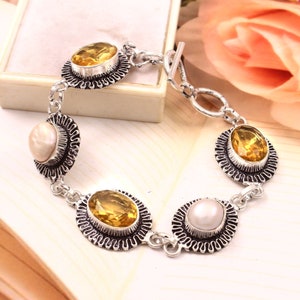 May include: A silver bracelet with four oval-shaped gemstones. Two of the gemstones are yellow citrine and two are white pearls. The bracelet has a toggle clasp.