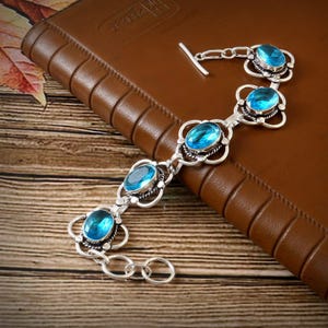 May include: A silver bracelet with four oval-shaped blue gemstones. The bracelet has a toggle clasp.