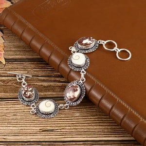 May include: A silver bracelet with five oval-shaped charms. The charms are decorated with a white and brown swirl pattern. The bracelet has a toggle clasp.