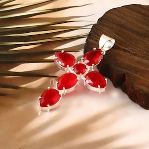 Puede incluir: Un colgante de cruz de plata con siete acentos de piedras preciosas rojas. El colgante está hecho de metal y tiene un acabado pulido.