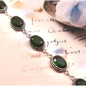 May include: A silver bracelet with five oval-shaped green gemstones. The bracelet has a delicate chain and small silver beads around each gemstone.