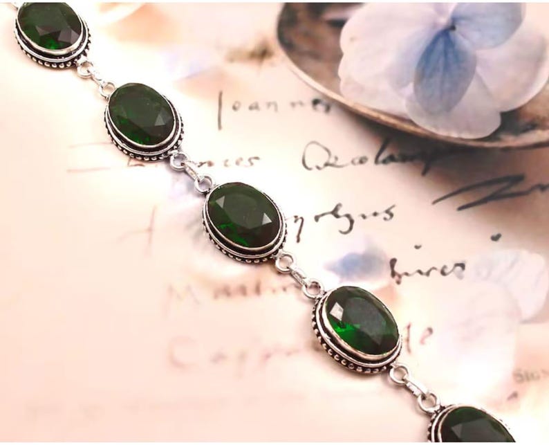 May include: A silver bracelet with five oval-shaped green gemstones. The bracelet has a delicate chain and small silver beads around each gemstone.