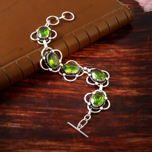May include: A silver bracelet with five green oval-shaped gemstones set in floral-shaped bezels. The bracelet has a toggle clasp.