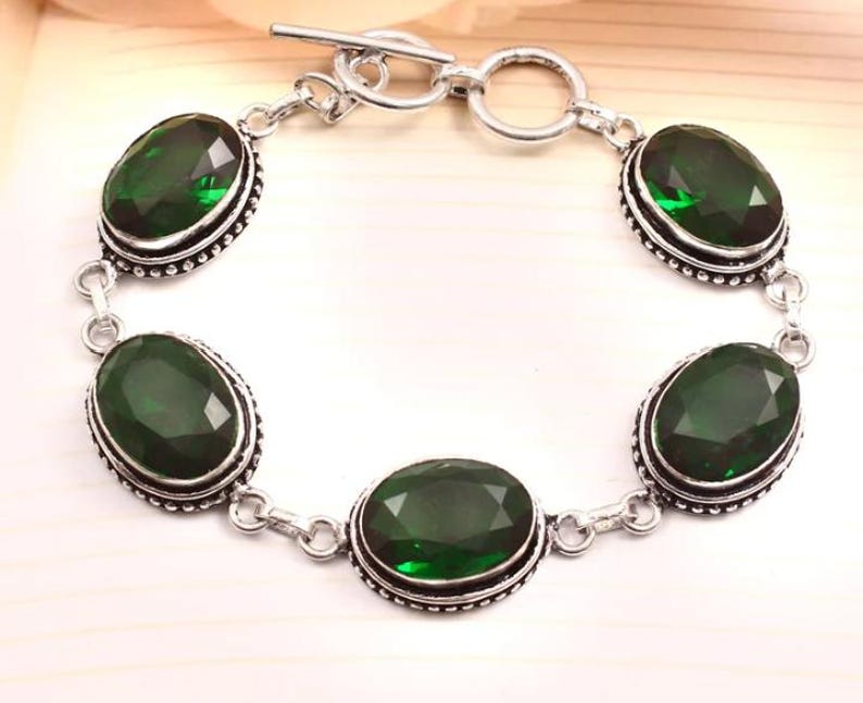 May include: A silver bracelet with four oval-shaped green gemstones. The bracelet has a toggle clasp.
