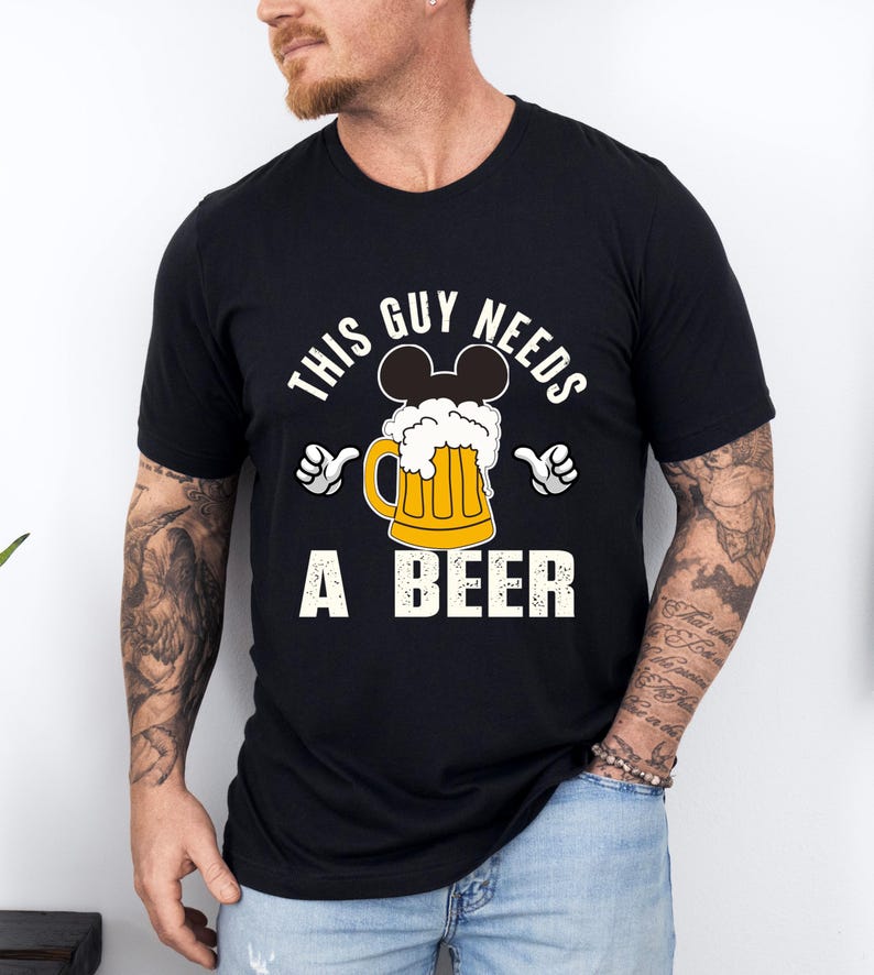 A man wearing a black t-shirt with a graphic design that says "This guy needs a beer" and features a beer mug with Mickey Mouse ears.