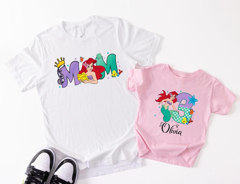 two t-shirts with the same design, one white and one pink, along with a pair of black and white sneakers.