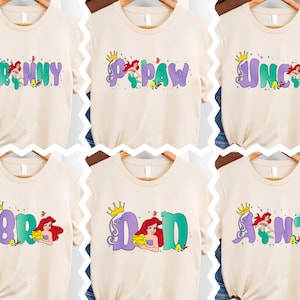 six different t-shirts with the same design, featuring the character Ariel from the Disney movie "The Little Mermaid". The design includes the character's name in a stylized font, along with various decorative elements such as crowns and other elements associated with the character's character.