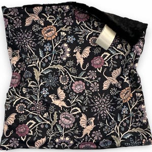 May include: A black fabric item with a floral and dragon pattern. The design features dragons, flowers, and foliage in shades of pink, peach, and blue against a black background. The item has a soft, black, furry lining.