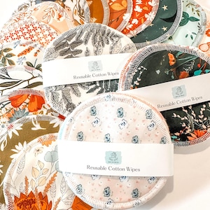 May include: A collection of reusable cotton wipes with various floral patterns in shades of orange, green, and white. The wipes are round with stitched edges and are held together with a white band that reads "Reusable Cotton Wipes".