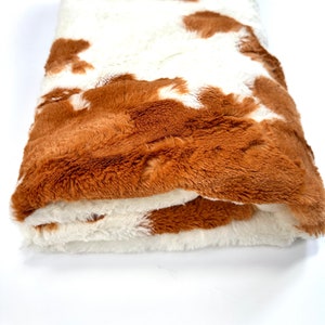 May include: A brown and white faux fur throw blanket with a cowhide pattern.