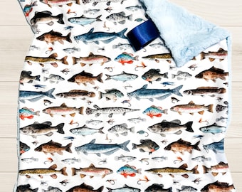 May include: A white baby blanket with a blue and white fish pattern. The blanket is made of soft, plush fabric and has a blue satin ribbon attached.