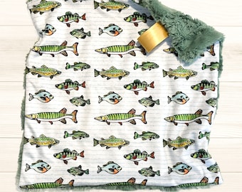 May include: A white baby blanket with a green plush border features a repeating pattern of colorful fish on a white background with thin blue stripes.