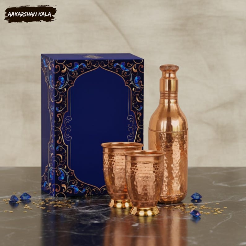 May include: A copper water bottle, two copper cups, and a gift box with a blue and gold design. The bottle and cups have a hammered texture. The gift box is dark blue with an arched design.
