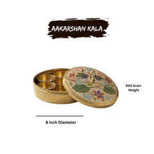 May include: A brass spice box with a lid featuring a peacock design. The box is 8 inches in diameter and weighs 900 grams. The text "AAKARSHAN KALA" is displayed above the box.