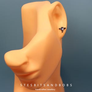 Peut inclure: Gros plan sur une oreille avec un piercing d'oreille en argent et bleu avec une petite pierre pr&eacute;cieuse. Le piercing est un design d&eacute;licat en trois parties avec une petite pierre pr&eacute;cieuse ronde au centre.