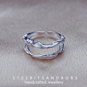 May include: Two silver rings with a twisted, organic design. The rings are stacked on top of each other, creating a unique and modern look.  The rings are handcrafted and made of sterling silver.