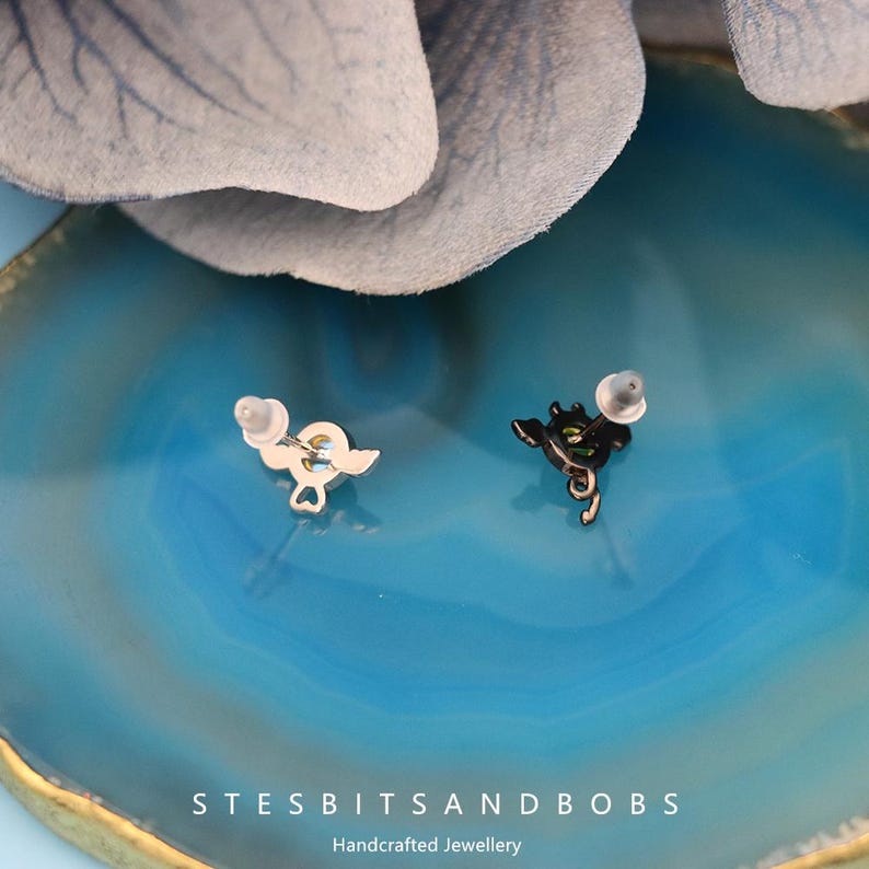 Peut inclure: Une paire de boucles d'oreilles en argent avec un motif de c&oelig;ur noir et blanc. Les boucles d'oreilles sont sur un fond bleu.