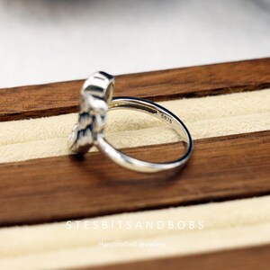 May include: A sterling silver ring with a detailed feather design. The ring is marked with "S925" on the inside of the band. The ring is displayed on a wooden surface. The text "STESBITSANDBOBS" and "Handcrafted Jewellery" are visible.