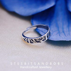 Peut inclure: Une bague en argent avec un motif de cerf et de forêt. La bague est sur un fond bleu.