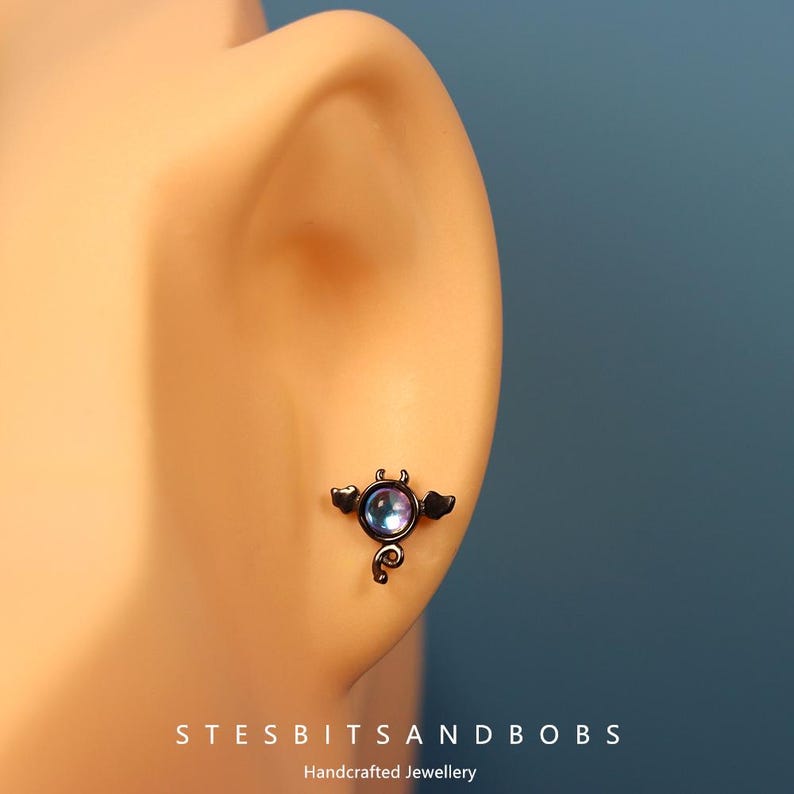 Peut inclure: Bijou de piercing de nez en forme de chauve-souris noire avec un gemme iridescent violet.