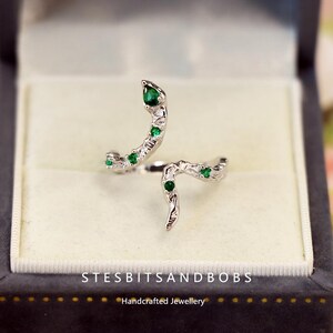May include: A silver ring featuring a green gemstone snake design. The ring is presented in a black ring box with the text "STESBITSANDBOBS Handcrafted Jewellery".