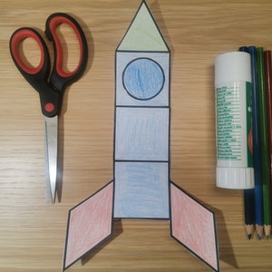 May include: A paper rocket craft with a green top, blue body, and red wings. The rocket is made of paper and has been coloured in with crayons.