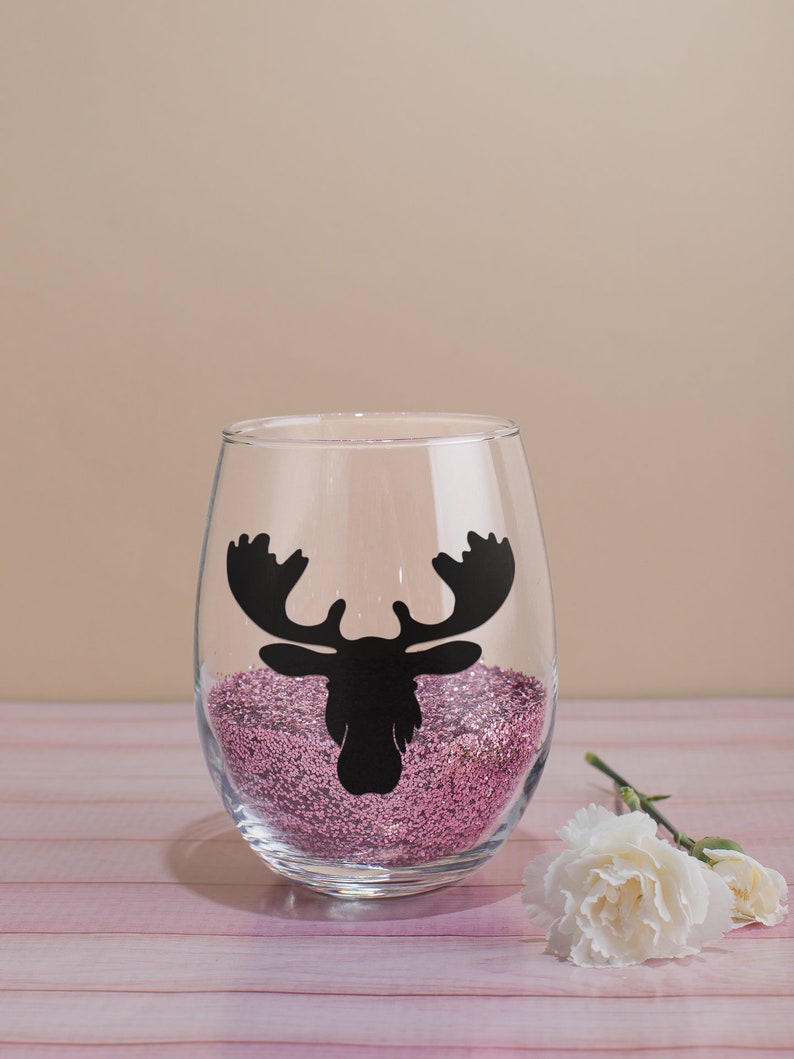 May include: A clear glass wine glass with a pink glitter base and a black moose silhouette decal.