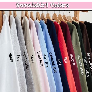 May include: A display of sweatshirts in various colors, including white, ash, sports grey, sand, light pink, light blue, Carolina blue, navy, red, maroon, military green, forest green, dark chocolate, and black.